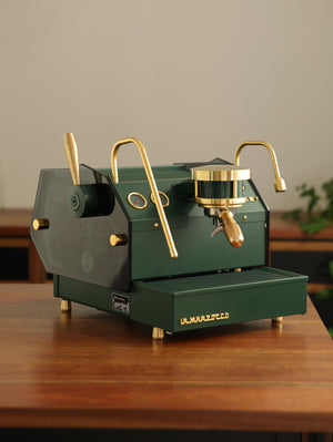 A deep green Specht La Marzocco GS3 with precision-machined brass and toughened dark glass side panels.